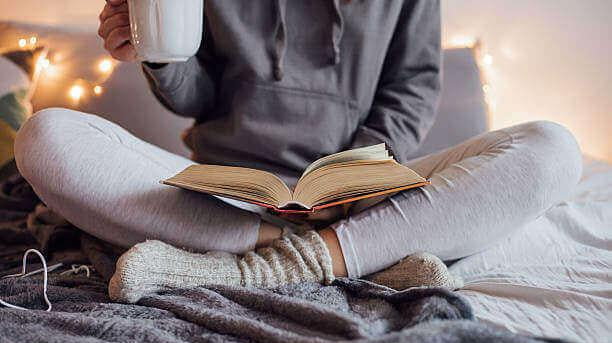 Woman sitting in bed drinking tea reading a book
