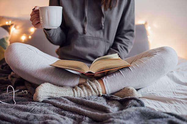 Woman sitting in bed drinking tea reading a book