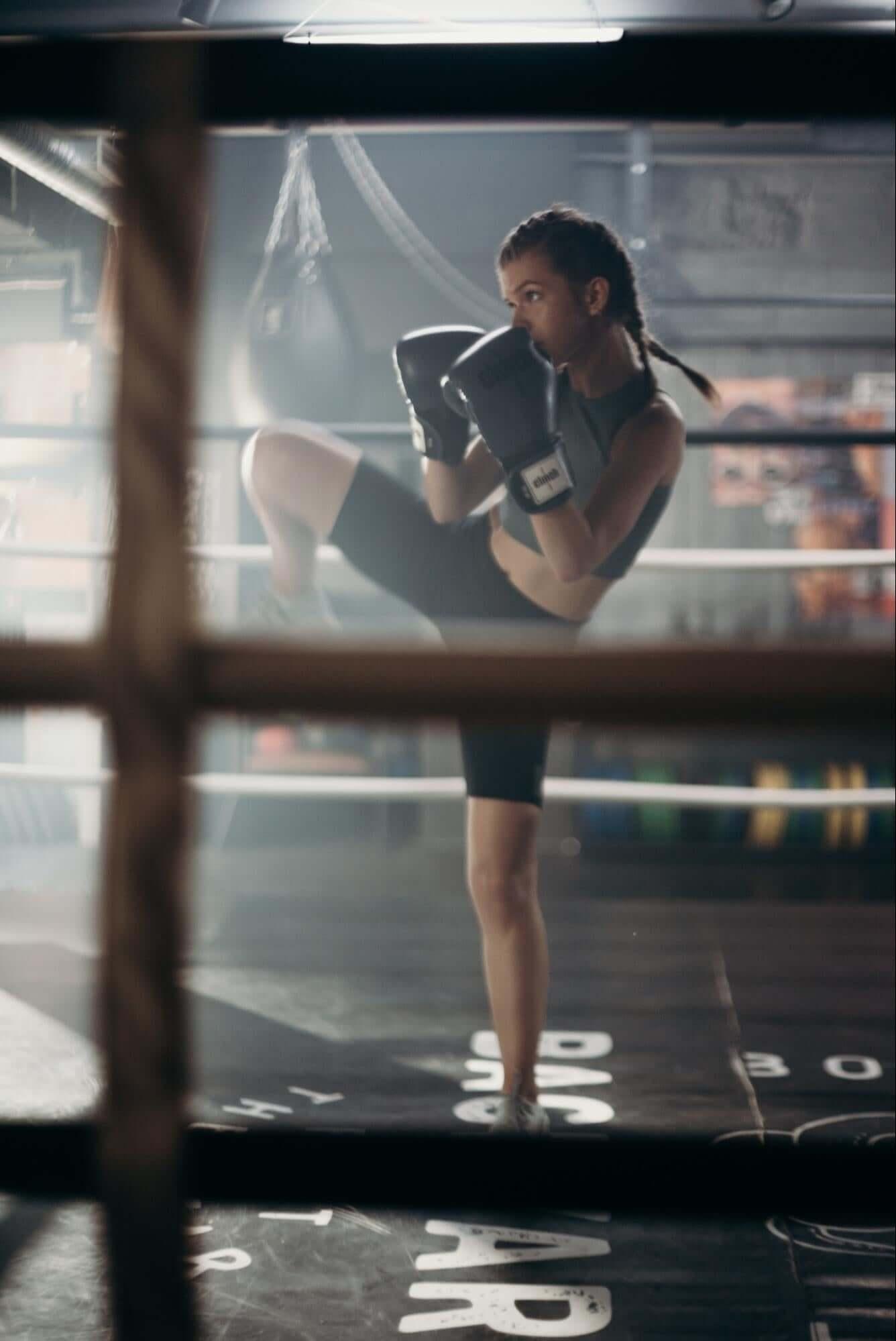 woman doing exercise in a boxing ring while wearing boxing gloves and exercise clothes