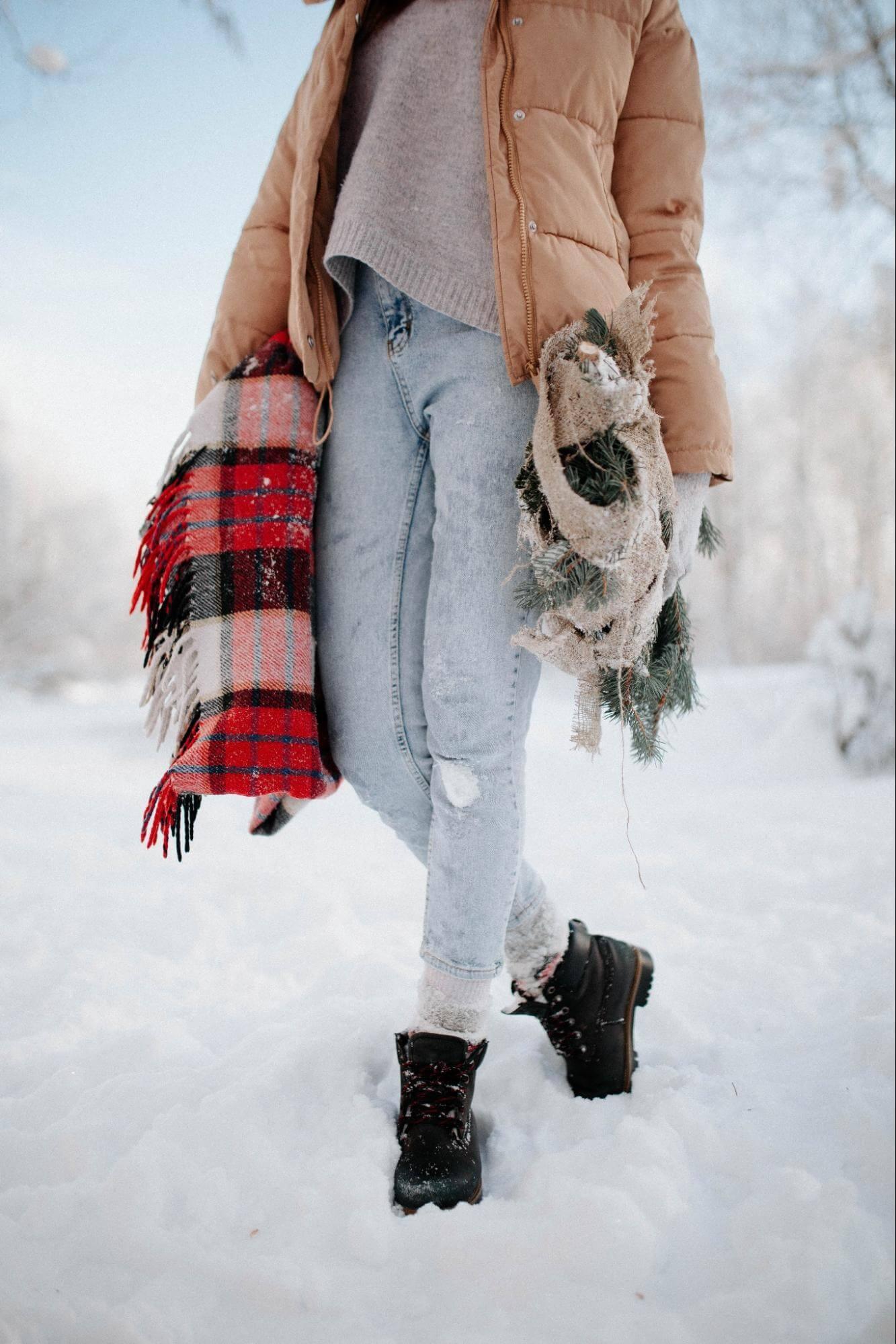 Alt Text: Woman in the snow with warm layers on carrying blankets